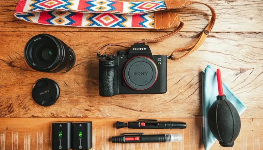 Un set da fotografia flat lay: fotocamera Sony, obiettivo, batterie, cinghia colorata e accessori per la pulizia.