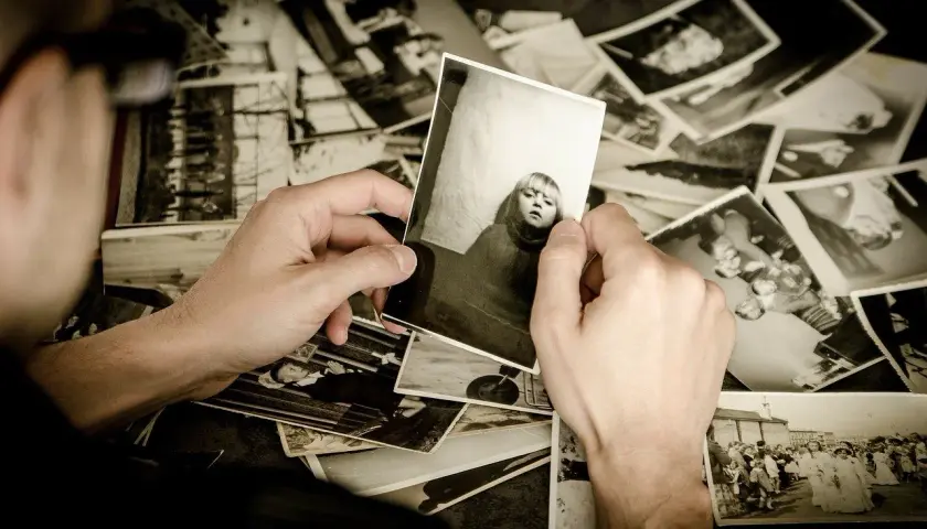 Mani che sfogliano un archivio foto, tenendo in mano una foto di una bambina. Ricordi che riaffiorano.