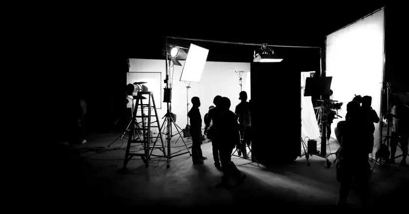 Scena di un set cinematografico con persone in silhouette, telecamere e un'intensa foto con luce.