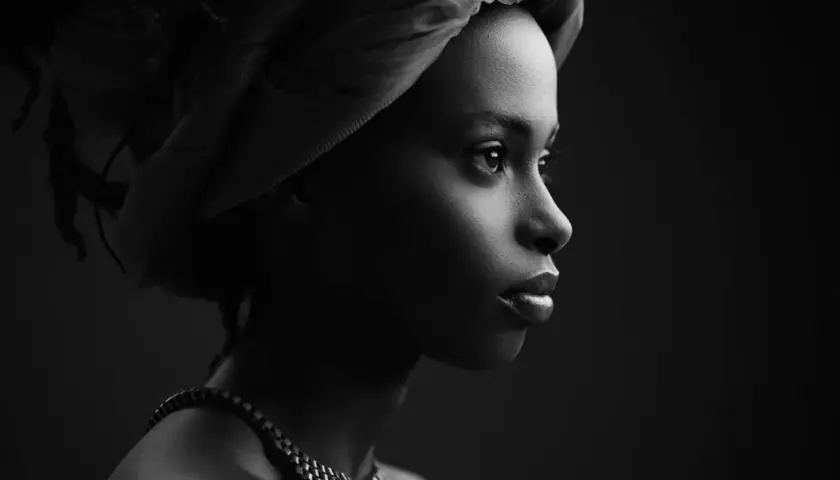 Ritratto low key di una donna con turbante e collana, illuminata da un lato, con uno sguardo intenso verso l'orizzonte.