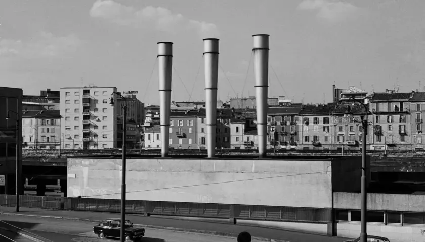 Gabriele Basilico foto: tre ciminiere svettano su un paesaggio urbano con palazzi e auto.