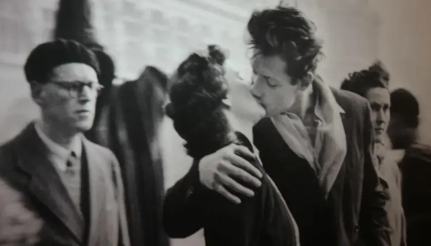 Un bacio appassionato catturato in uno degli iconici robert doisneau opere. Un uomo con berretto e occhiali osserva la scena.