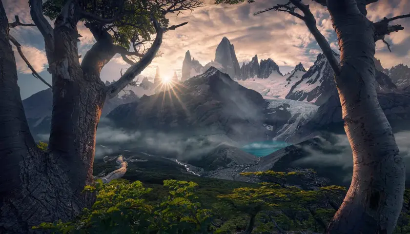 Alba dorata sui picchi innevati del **max rive**, con un lago turchese e alberi antichi in primo piano.