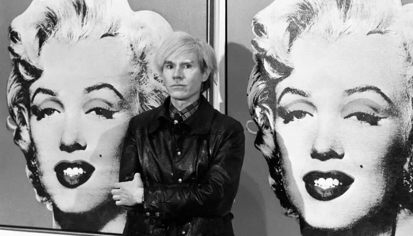 Andy Warhol posa tra i suoi iconici ritratti di Marilyn Monroe, un'immagine che definisce la Pop Art.
