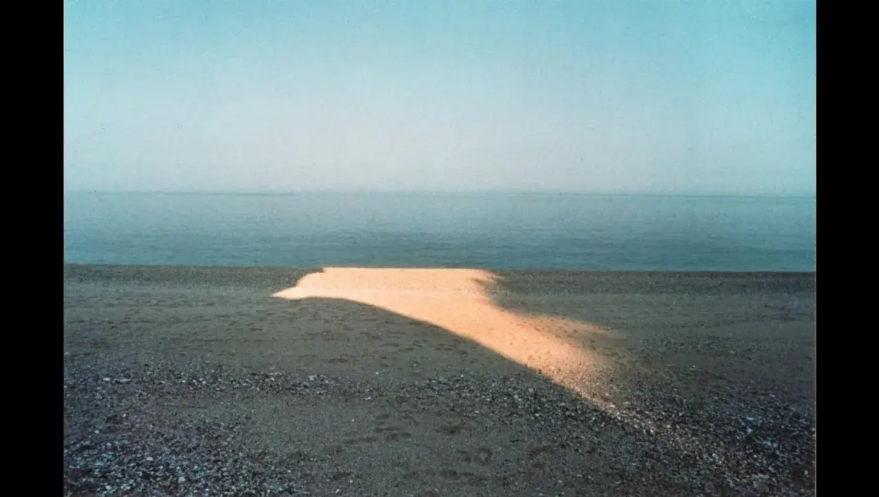 Una spiaggia con un'onda di luce dorata che attraversa la sabbia, tipica di una franco fontana foto. Il mare calmo e il cielo azzurro completano la scena.