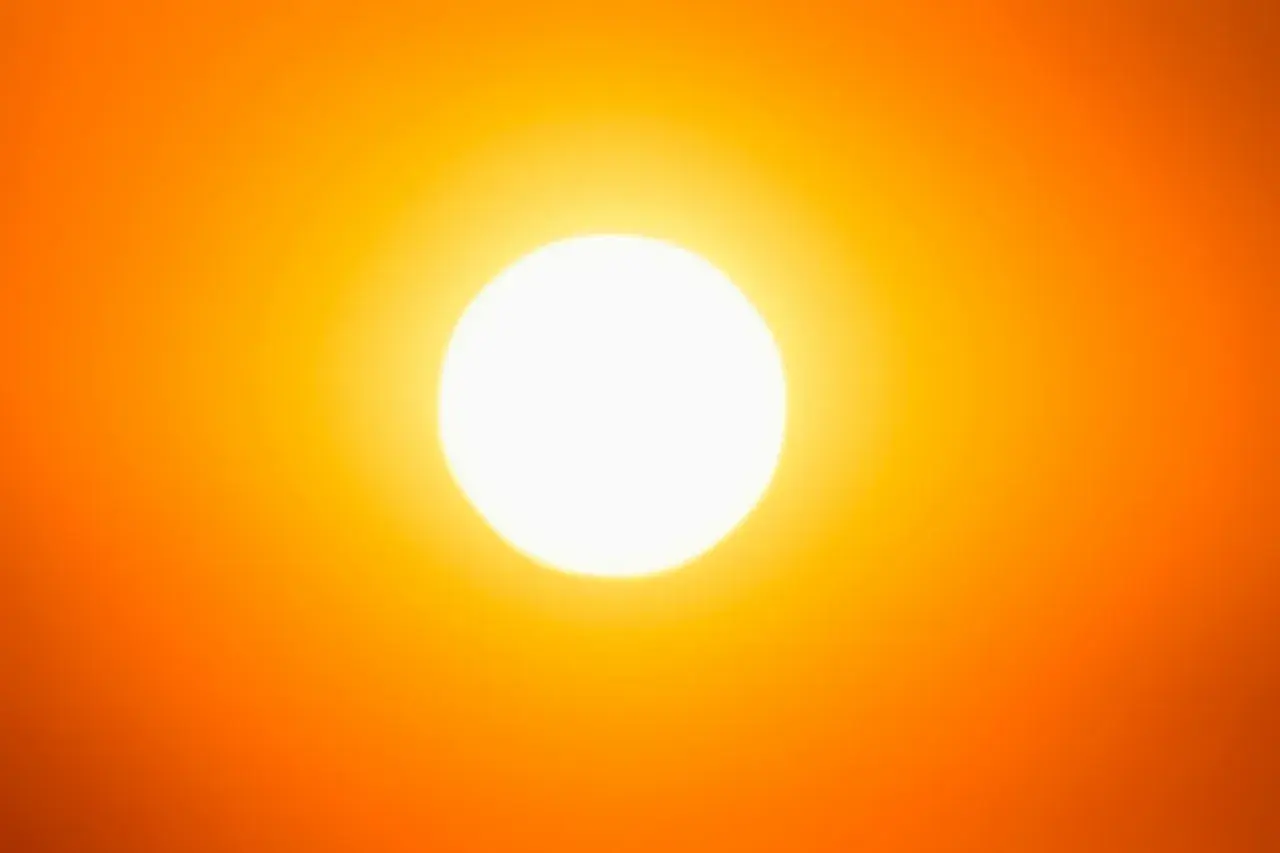Una foto al sole, con un bagliore intenso che illumina un cielo arancione.