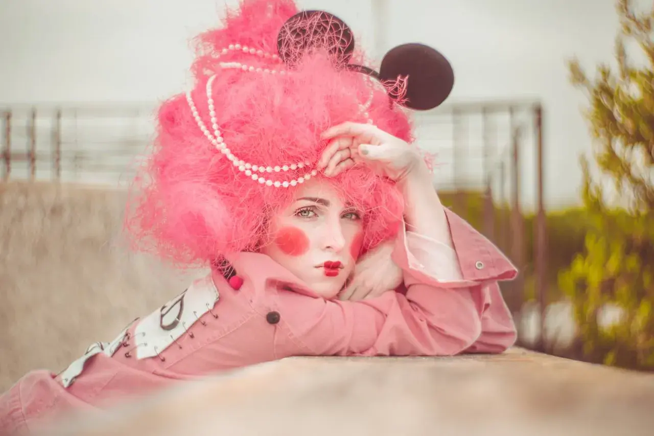 Modella con parrucca rosa shocking, trucco da clown e orecchie da topo. Un'idea per foto stravagante e colorata.