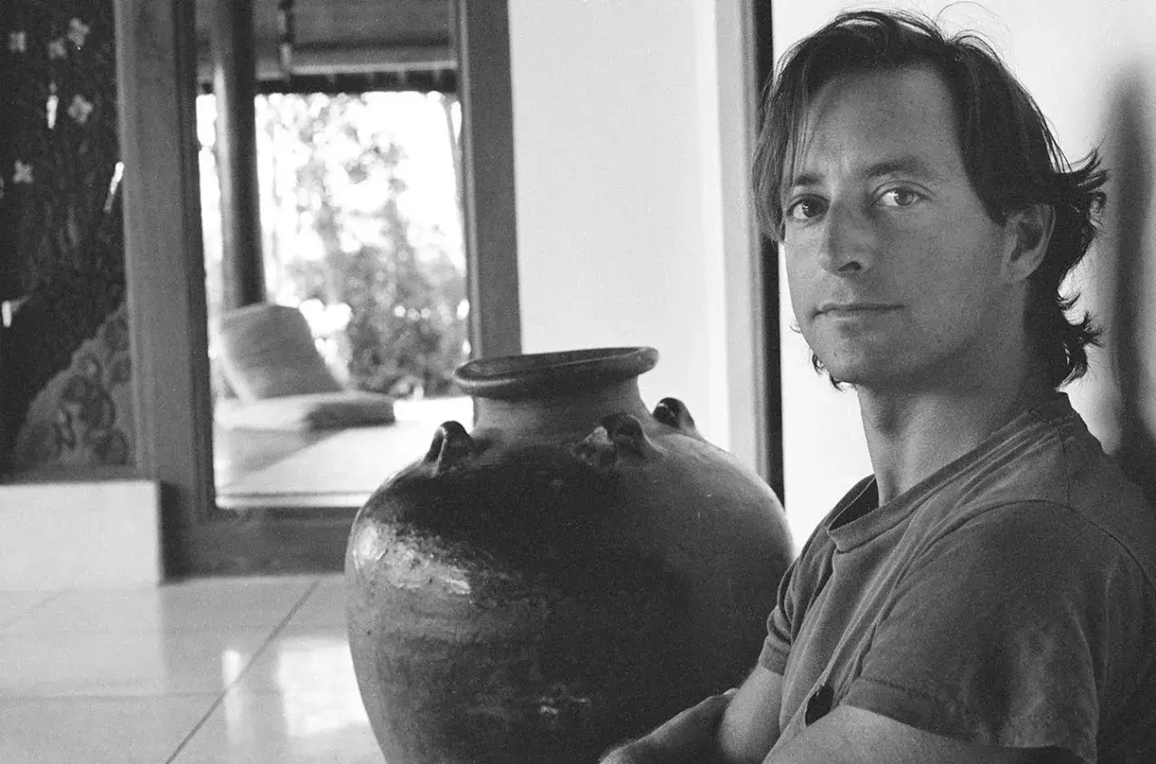 Ritratto di Herb Ritts accanto a un'antica giara, con uno scorcio di un salotto in stile tropicale sullo sfondo.