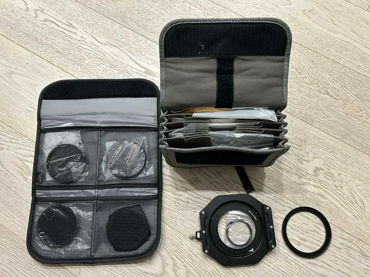 Custodia aperta con vari filtri fotografici rotondi e quadrati, un porta filtro e un anello adattatore.