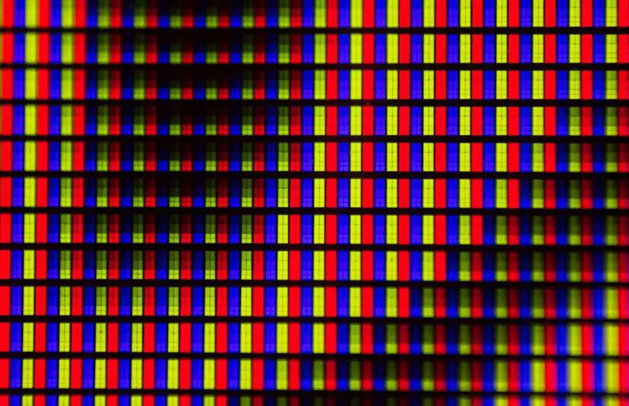 Primo piano di una griglia di pixel RGB. Ogni pixel è composto da sottili barre verticali rosse, verdi e blu, che creano un effetto visivo vibrante, quasi un hot pixel.