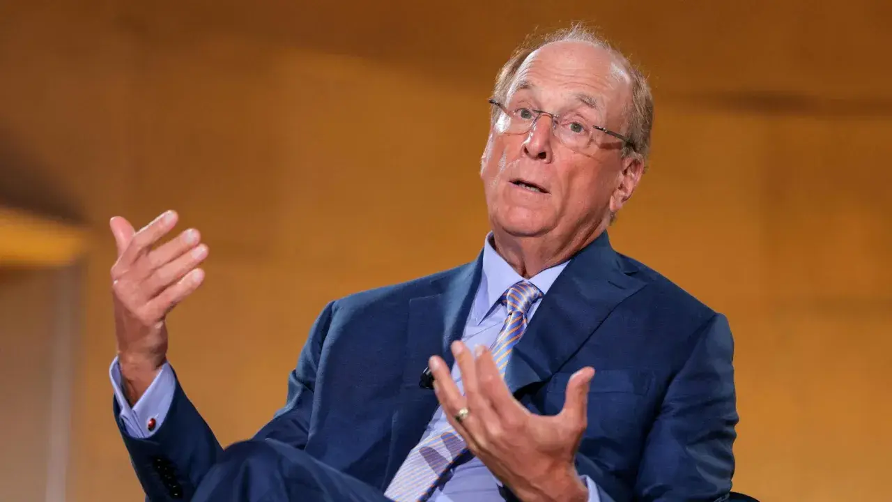Larry Fink, il fotografo, parla con le mani. Indossa un abito blu e una cravatta a righe.