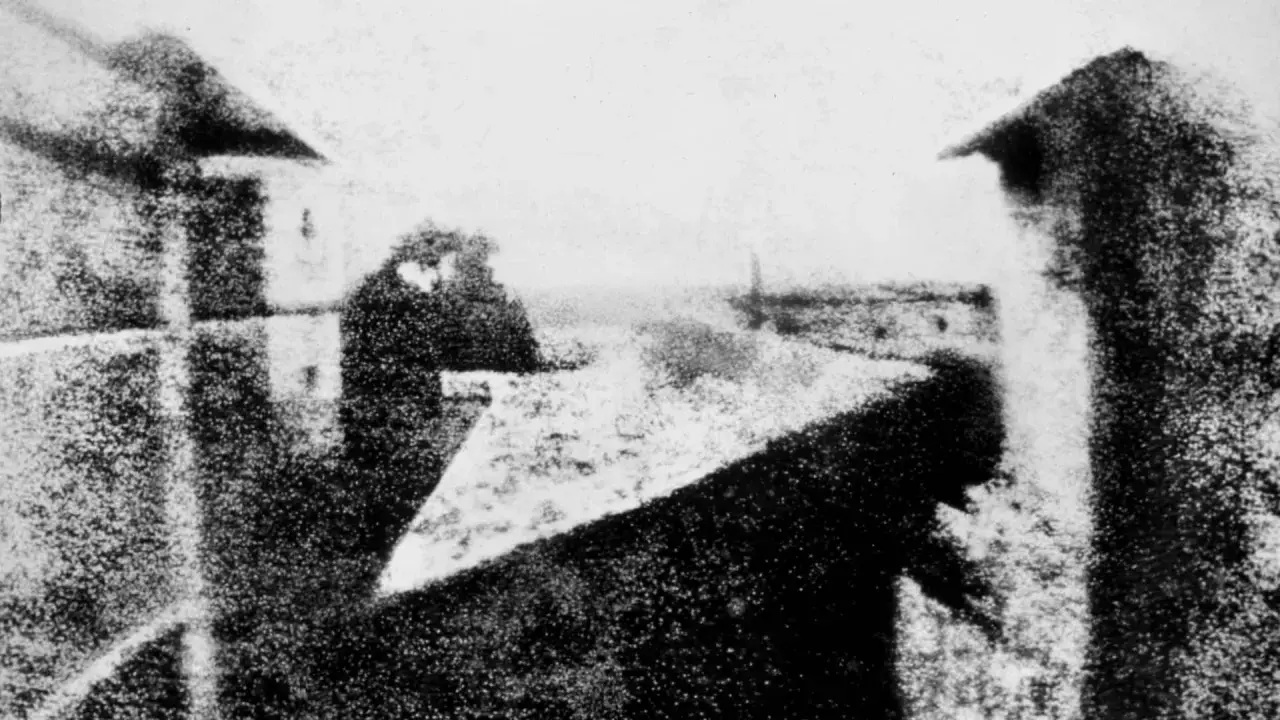 La prima foto della storia: una vista da una finestra, con figure sfocate e un paesaggio urbano lontano.