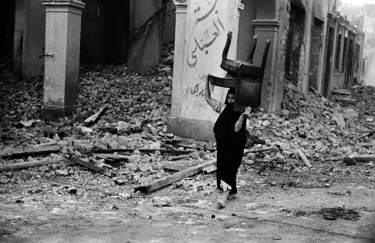 Una donna con un velo nero porta una sedia tra le macerie, un'immagine potente di resilienza catturata da David Seymour.