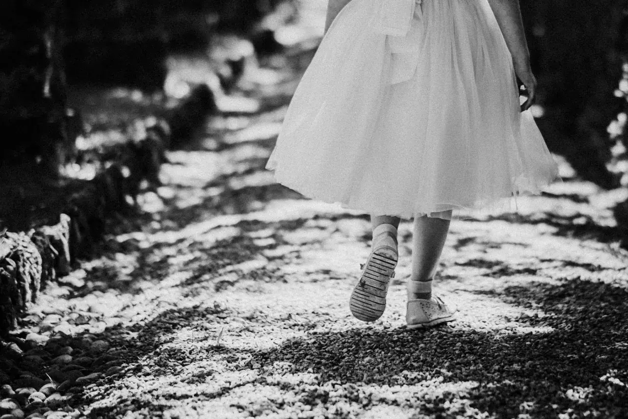 Bambina con vestito bianco cammina su un sentiero di ghiaia. Emozioni fotografie bellissime bianco e nero catturano la sua innocenza.