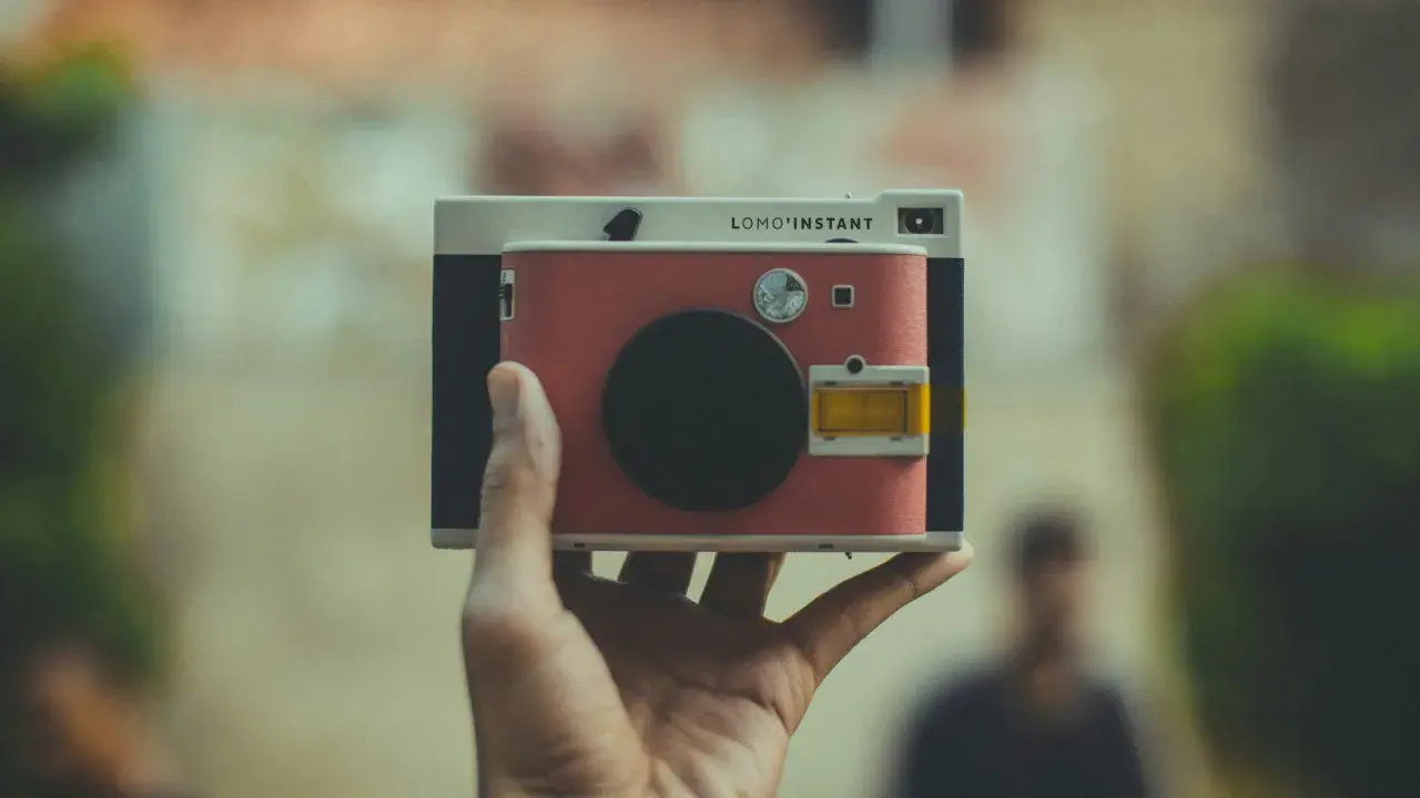 Una mano tiene una Lomo'Instant. Cosa significa "fotocamera ai"? Questa fotocamera istantanea, con il suo design retrò, cattura momenti unici.