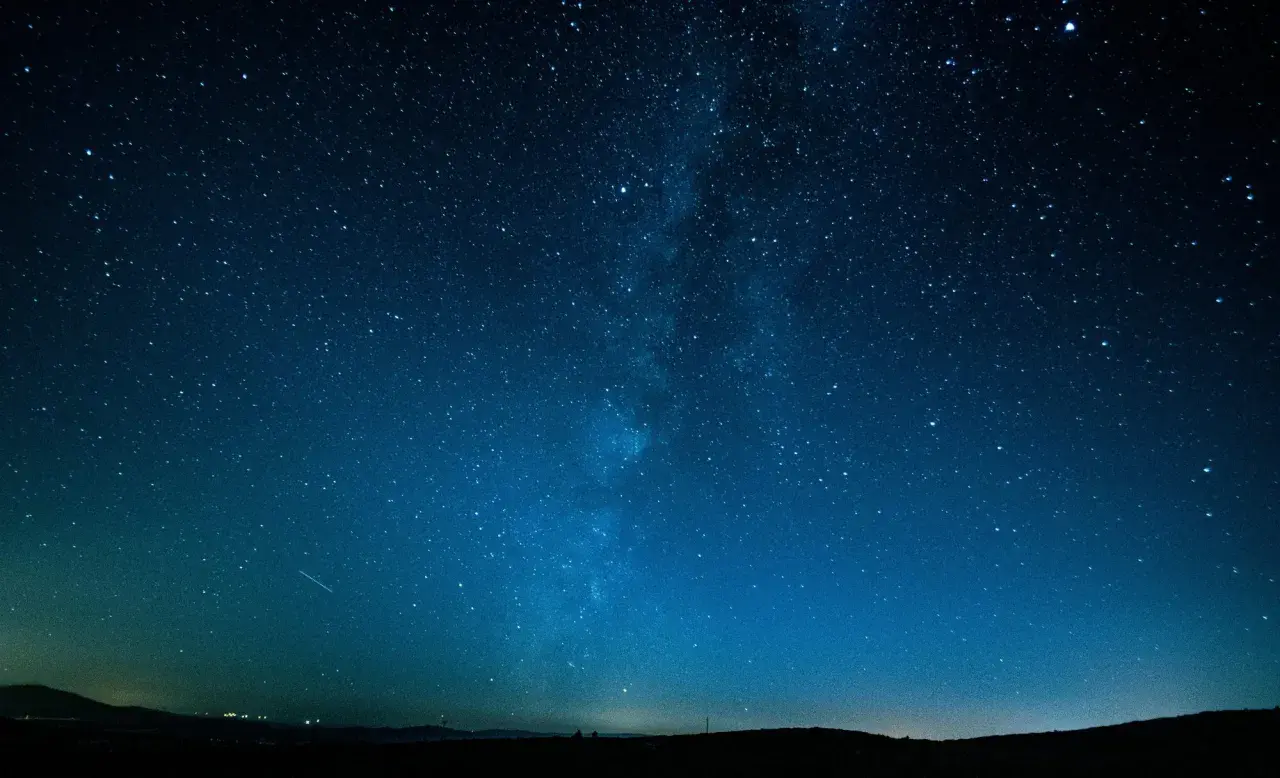 Cielo stellato blu intenso, con la Via Lattea visibile. Un'impresa di fotografare di notte a mano libera, con un leggero bagliore all'orizzonte.