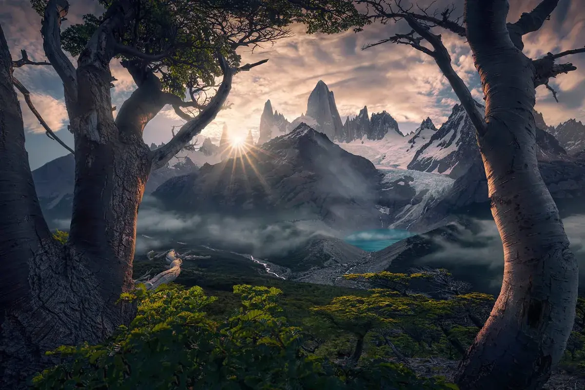 Alba dorata sui picchi innevati del **max rive**, con un lago turchese e alberi antichi in primo piano.