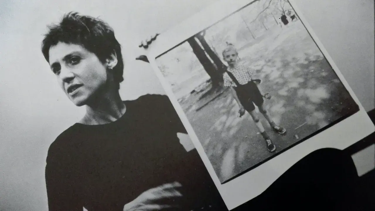 Diane Arbus, con la sua inconfondibile espressione, tiene in mano una delle sue celebri fotografie: un bambino in un parco.