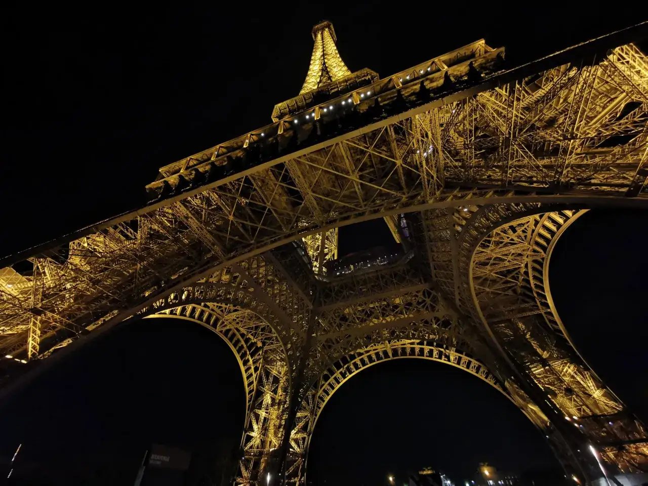 La Torre Eiffel illuminata di notte, catturata con la fotocamera Huawei P30 Pro, mostra la sua imponente struttura metallica dorata contro il cielo scuro.