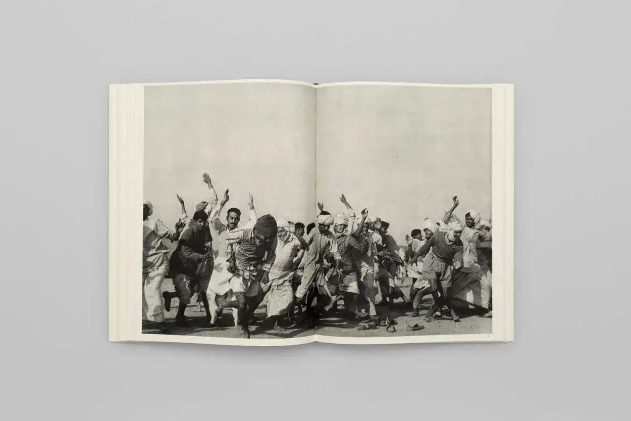 Un gruppo di uomini in turbante corre con le braccia alzate, un'istantanea dinamica catturata da Cartier-Bresson.