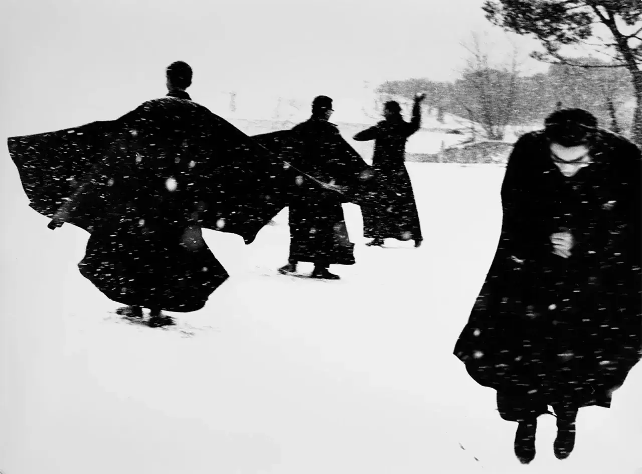 Mario Giacomelli: pretini in movimento nella neve, silhouette scure contro il bianco, un'atmosfera quasi eterea.