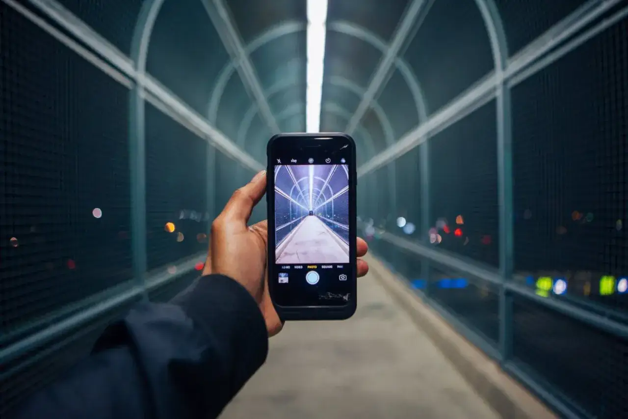 Una mano tiene un cellulare che scatta una foto a un tunnel futuristico illuminato.