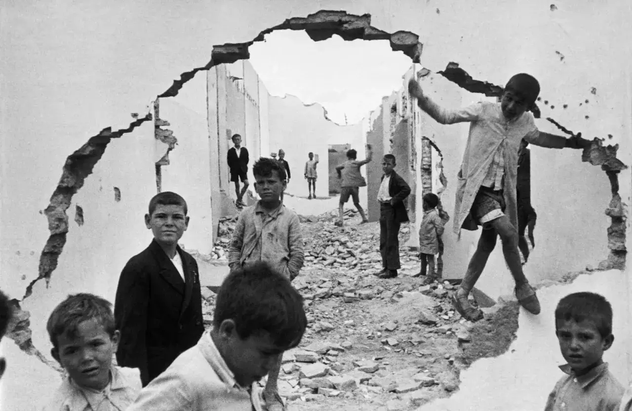 Un'opera d'arte di Henri Cartier-Bresson: bambini giocano tra le macerie di un muro crollato, un'istantanea di resilienza e innocenza.