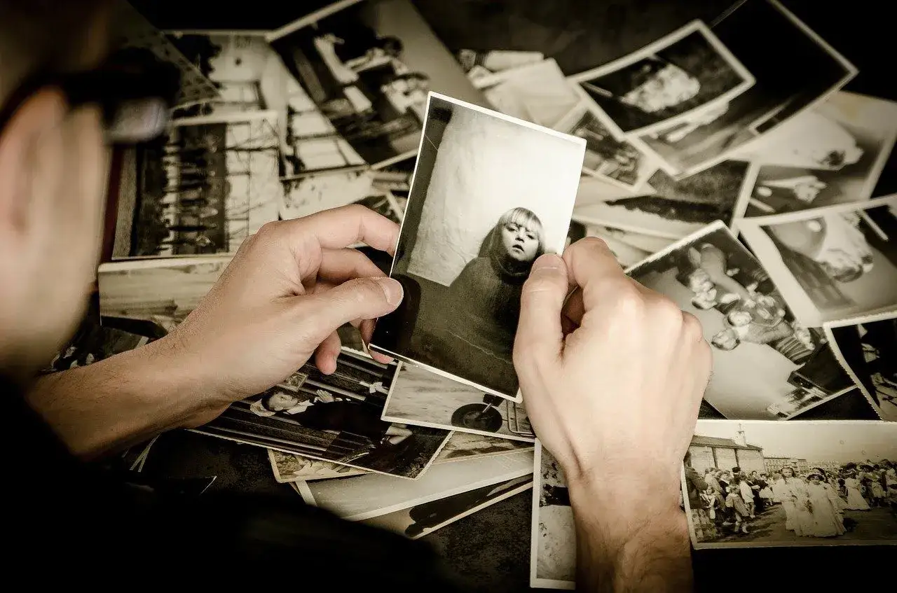 Mani che sfogliano un archivio foto, tenendo in mano una foto di una bambina. Ricordi del passato riaffiorano tra vecchie immagini.