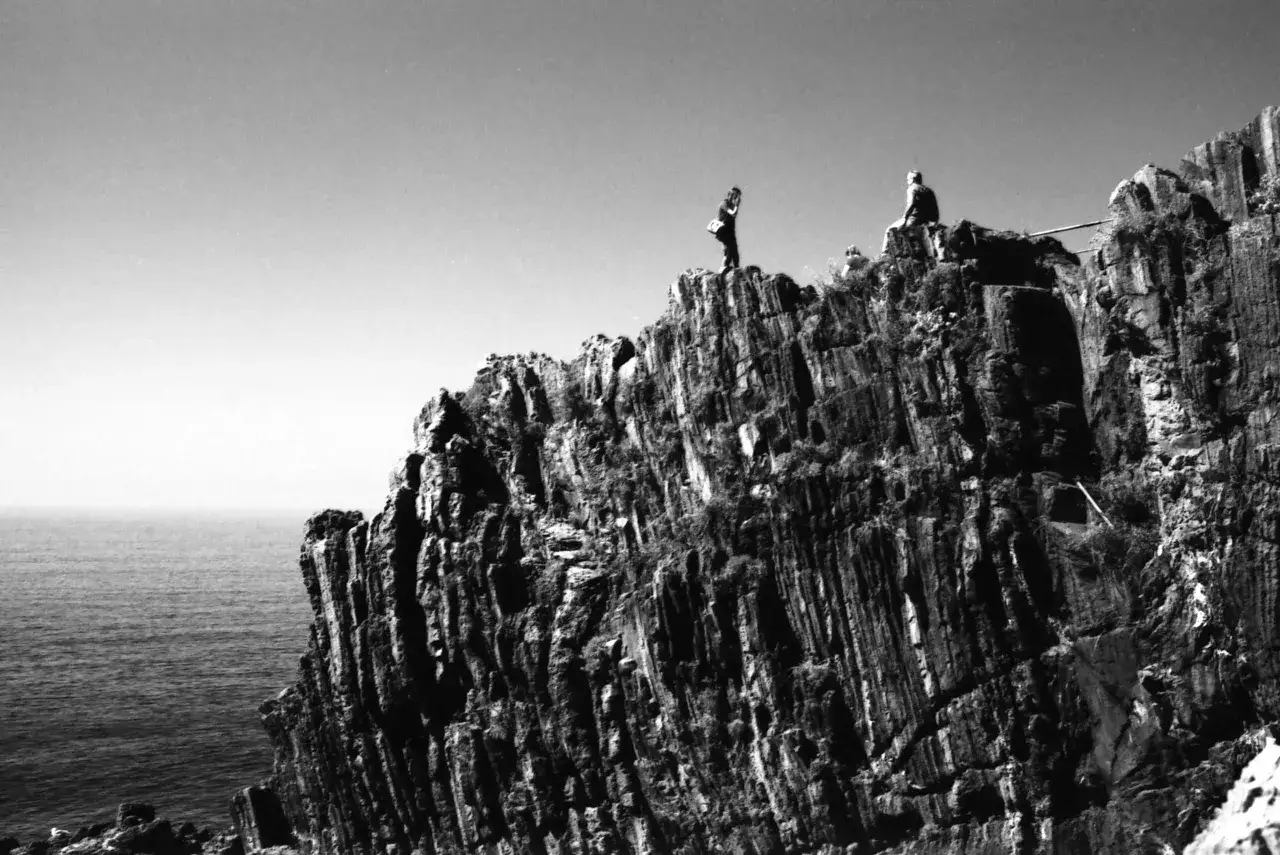 Due persone su una scogliera a picco sul mare, la roccia mostra un evidente sistema zonale.