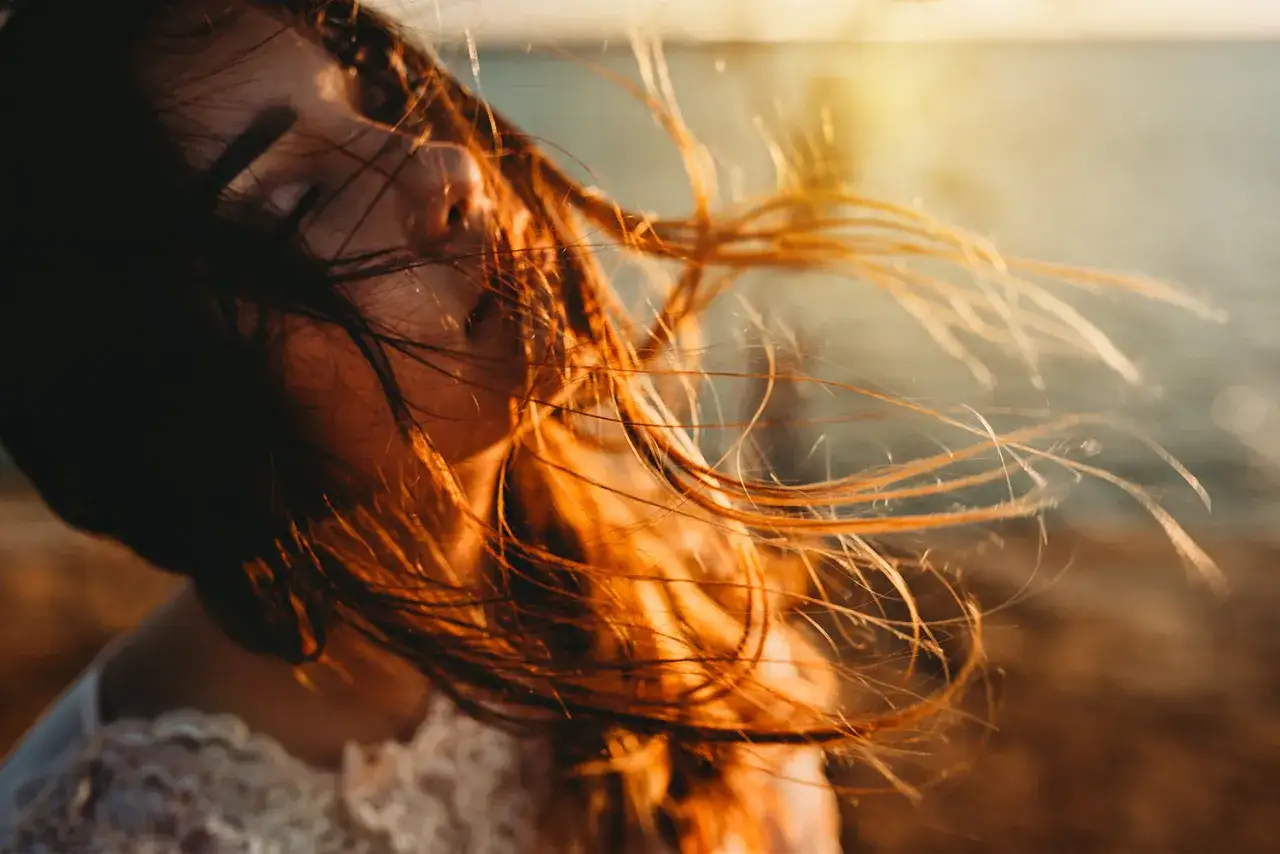 Ragazza con capelli mossi dal vento, immersa nella luce calda del golden hour, che evoca un senso di pace e libertà.