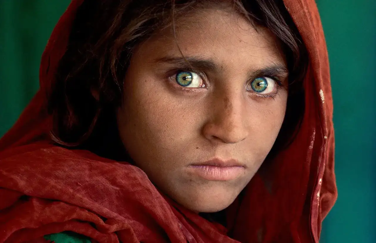 Occhi penetranti di una giovane ragazza afghana, resi celebri da Steve McCurry, incorniciati da un velo rosso.