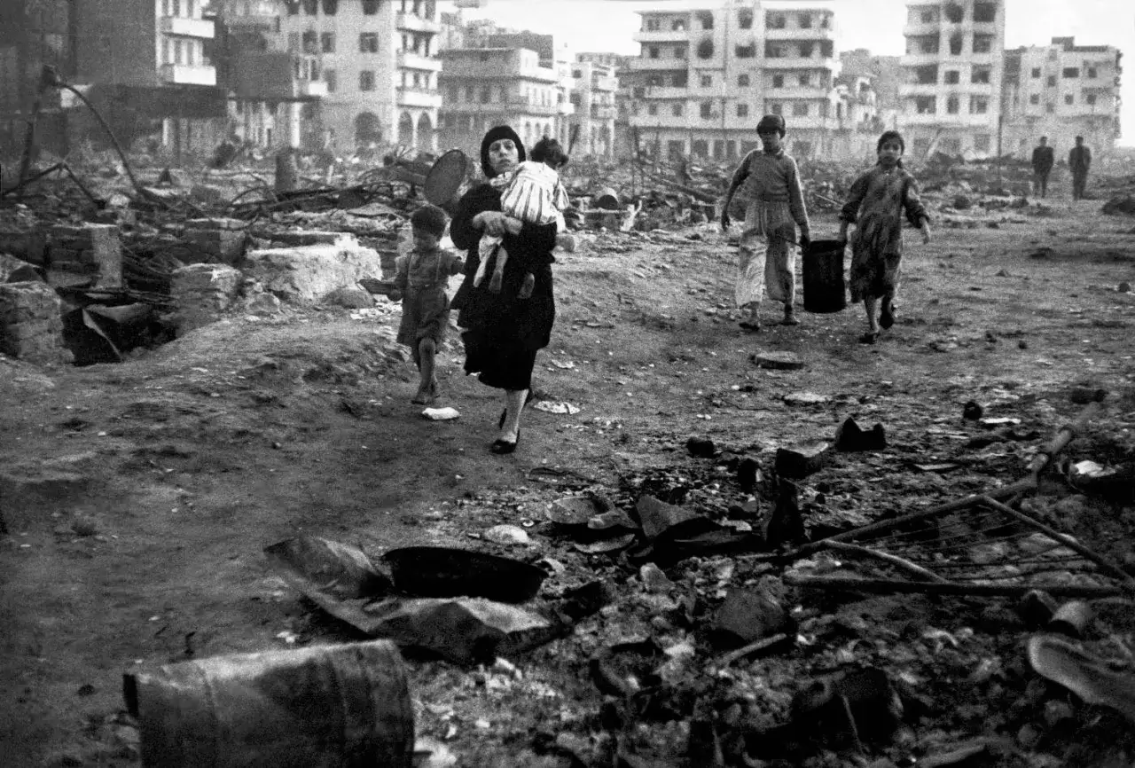 Una madre con un bambino in braccio attraversa un paesaggio devastato, un'immagine potente di David Seymour.