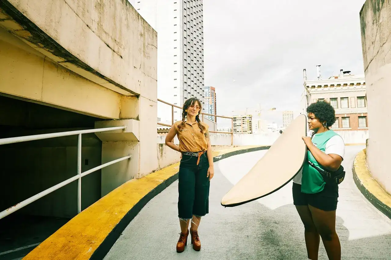 Due ragazze con una tavola da surf, in una foto al sole su un tetto con vista sulla città.